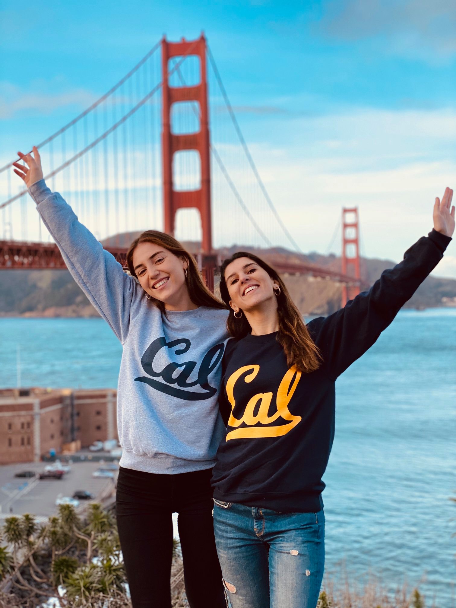 Two students in UC sweatshirts smiling in front of the Golden Gate Bridge